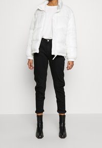 Biała kurtka puchowa z wysokim kołnierzem, z zapięciem na zamek i elastycznymi mankietami. W połączeniu z czarnymi dopasowanymi dżinsami i czarnymi botkami na kostkę.