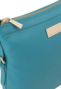 Groene leren clutch met een gestructureerde afwerking, voorzien van een gouden ritssluiting en een merkembleem. De afmetingen zijn slank en rechthoekig.