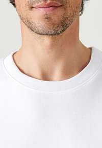 T-shirt bianco in cotone con scollatura rotonda e dettagli a coste, che presenta una texture liscia e cuciture pulite attorno al colletto.
