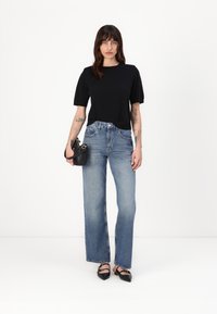 Schwarzes kurzärmliges Oberteil kombiniert mit hellblauen weiten Jeans mit leichtem Verblassen, abgerundet durch schwarze spitze Schuhe und eine schwarze Tasche.