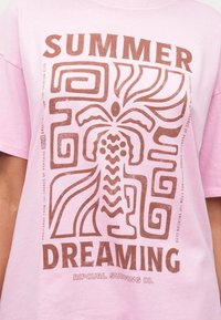 Pink t-shirt featuring a large, brown graphic with abstract patterns and the text "SUMMER DREAMING" in bold. Soft cotton texture.
