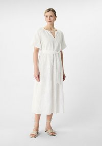 Weißes Maxikleid mit floraler Stickerei, V-Ausschnitt, kurzen Puffärmeln und einem gebundenen Gürtel an der Taille. Getragen mit beigen Riemchensandalen.