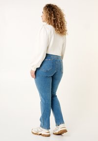 Blouse légère à manches bouffantes associée à un jean bleu taille haute. Le jean a une coupe classique et comporte des poches arrière. Porté avec des baskets blanches.