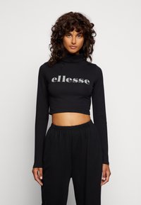 Juodas ilgas rankovės trumpas megztinis su imitacine apykakle; ant krūtinės turi pilką "ellesse" logotipą. Lygus, tamprus audinys. Derinamas su juodomis kelnėmis.
