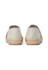 Krémszínű vászon espadrilles fekete díszítéssel, fonott juta talppal. A dizájn alacsony profilú, lekerekített hátrésszel rendelkezik.