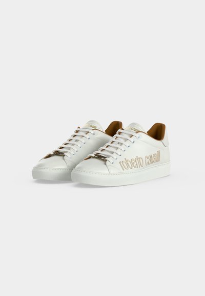 Paire de baskets basses blanches avec lacets blancs, intérieur beige clair, et "roberto cavalli" brodé en beige sur le côté.
