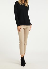 Schwarzer Pullover mit langen Ärmeln, kombiniert mit beigefarbenen, eng anliegenden Hosen und schwarzen Stiefeletten. Glatte Textur, minimalistisches Design.