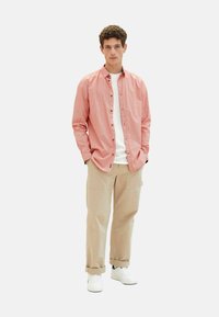 Rot gemusterte Hemd mit Knöpfen, darunter ein weißes T-Shirt, beiges Cargo-Hosen und weiße Sneaker; jugendlicher Schnitt und lässiger Stil.