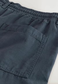Section de shorts en tissu gris foncé montrant une ceinture élastique et une poche arrière carrée avec des coutures détaillées.