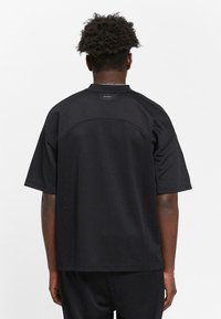 Men's black athletic shirt made of perforated material, featuring short sleeves, a round neckline, and a label at the neck. Textured surface visible.