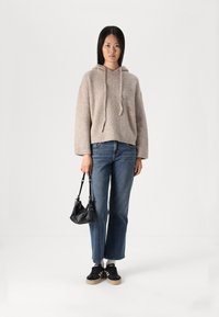 Felpa beige lavorata a maglia con coulisse, abbinata a jeans blu a gamba dritta. Borsa nera con tracolla a catena, sneakers nere con suola beige.