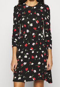 Czarna sukienka do kolan z rękawami o długości trzech kwart, ozdobiona czerwonymi, białymi i różowymi wzorami kwiatowymi oraz lekko dopasowaną talią.