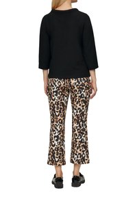 Zwarte textuur top met 3/4 mouwen, gecombineerd met cropped broeken met een luipaardprint in bruin- en zwarttinten, gedragen met zwarte schoenen.