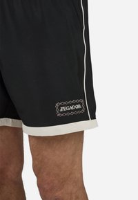 Shorts de sport noirs avec des détails blancs, portant une étiquette brodée "PEGADOR". Fabriqués en tissu lisse, coupés au genou.
