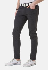 Dunkelgraue Slim-Fit-Jeans mit strukturiertem Muster, fünf Taschen und einem weißen Gürtel. Kombiniert mit weißen Sneakers.