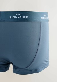 Námořnické modré pánské boxerky s jemnou, hladkou tkaninou, s kontrastním páskem označeným "NEXT SIGNATURE" v bílé barvě.