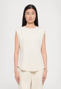 Light beige sleeveless top with a round neckline and shoulder pleats, featuring a smooth texture and slightly curved hemline.
