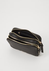 Clutch nera in pelle con zip e hardware dorato, presenta più scomparti e una finitura testurizzata. Forma arrotondata con una tracolla laterale.