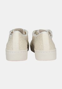 Zapatillas de lona crema con una superficie texturizada, suaves acentos en blanco y una suela de goma blanca de perfil bajo, vistas desde la parte trasera.