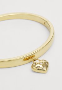 Goldener Armreif mit einem Herzanhänger, der Sternenmuster und kleine klare Steine aufweist. Glatte, polierte Oberfläche mit einfachem Design.