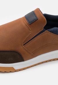 Zapato marrón de piel sin cordones con textura perforada, acentos en azul marino, una sección de ante suave y una suela de goma blanca con un diseño de tracción.