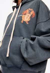 Granatowa bluza z kapturem wykonana z miękkiego materiału, z kieszenią kangurką, ozdobiona fantazyjnym nadrukiem jamnika oraz kremowymi sznurkami.