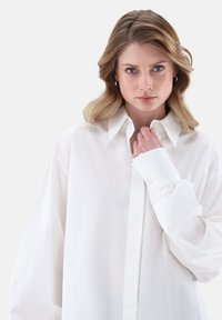 Weißes, oversized Hemd aus glattem Stoff, mit klassischem Kragen und Knopfleiste, lockeren, weiten Ärmeln und minimalistischem Design.