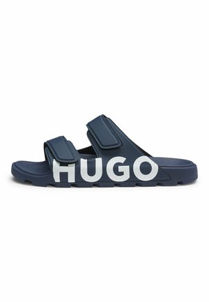 Navy slide sandal with two adjustable straps and large white "HUGO" text on the side of the sole.