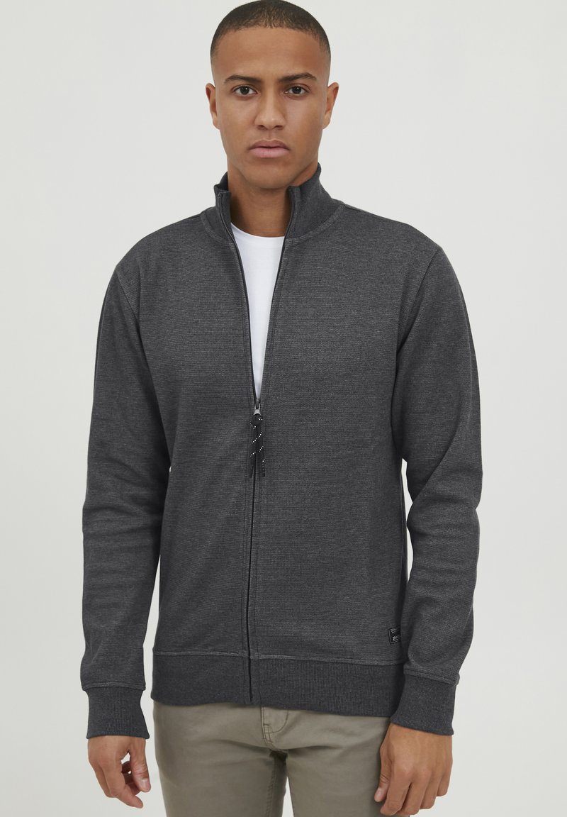 Tumši pelēks zip-up jaka mīkstā, teksturētā audumā. Iespējo augstu apkakli, priekšējo rāvējslēdzēju un ribotās aproces. Slim fit dizains ar logo uzrakstu.