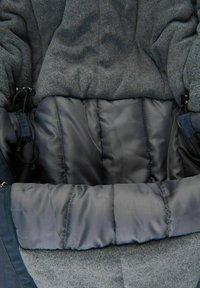 Chaqueta gris forrada con forro polar, con una textura exterior suave, que presenta un forro interior acolchado oscuro y cierres ajustables con cordones en los lados.