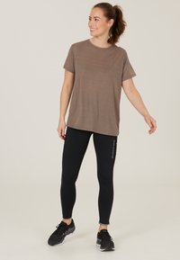 Ruskea, lyhythihainen, pyöreäkauluspaita yhdistettynä mustiin, istuviin leggingseihin, joissa on logo sivussa, ja mustiin urheilukenkien.