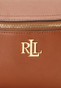 Ruskean keinonahkainen laukku, jossa on kultainen vetoketju ja suuri kultainen "RL"-logo. Sileä pinta ja tikkaukset.