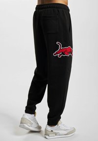 Svarta sweatpants med en broderad röd tjur-logotyp på vänster ben, med dragsko i midjan och elastiska muddar.