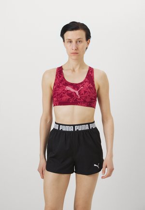 Sutien sport roșu cu imprimeu floral, cu decolteu rotund și logo. Şorturi sportive negre, cu un braț elastic lat, având textul și logo-ul "PUMA".