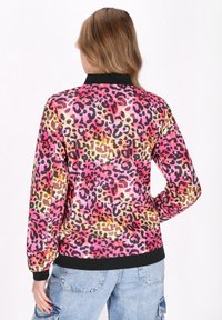 Jachetă cu imprimeu leopar, prezentând culori roz, portocalie și neagră, cu guler și manșete negre. Fabricată dintr-un material neted, cu o croială lejeră.