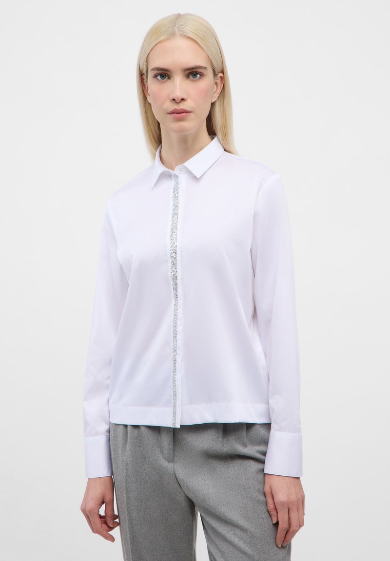 White long-sleeve shirt with a collar, featuring a central sequined accent, tailored fit, and smooth texture. Worn with grey trousers.