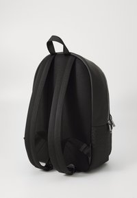 Sac à dos noir de forme arrondie, fabriqué avec des matériaux lisses et texturés. Il présente des bretelles rembourrées et une poignée supérieure pour le transport.