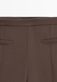 Pantaloni marroni da donna con passanti per cintura, parte anteriore liscia e tasche laterali con spacco, mostrati dalla vita a metà coscia.