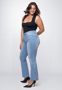 Helle blaue Schlagjeans mit hoher Taille, ausgestattet mit Fronttaschen, sanften Verwaschungen und Schlitzen am Saum, kombiniert mit einem schwarzen ärmellosen Oberteil.