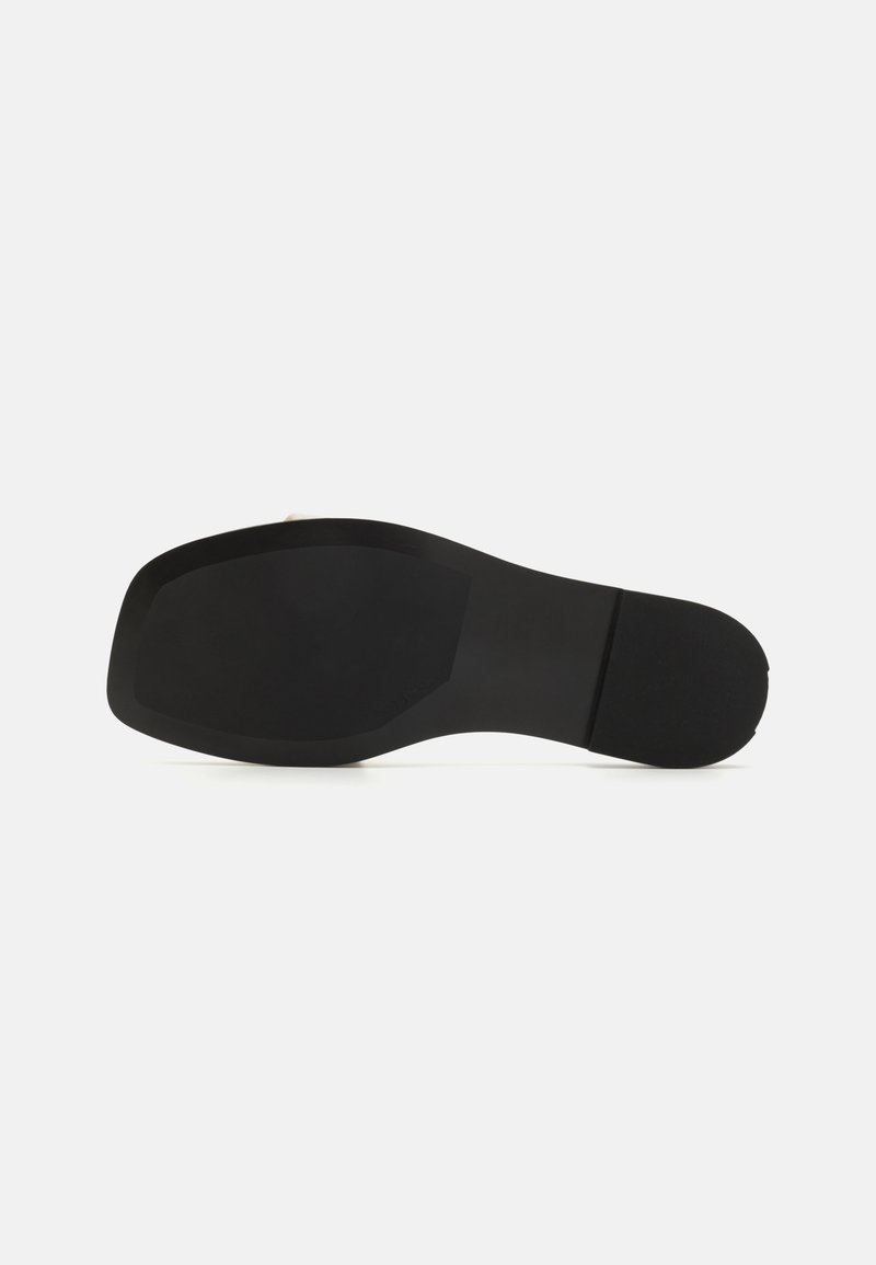 La semelle noire de la chaussure présente un design plat et lisse avec une légère courbure au niveau du talon. Elle est fabriquée en caoutchouc avec des motifs de grip texturés.