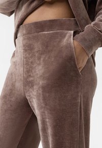 Fluweelzachte bruine broeken met een gladde textuur, voorzien van een zijzak en een brede elastische tailleband voor comfort.