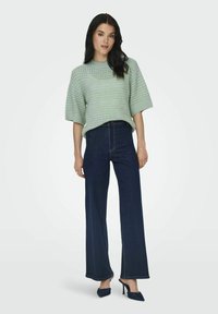 Maglione a maglia verde menta con maniche corte, abbinato a jeans a vita alta blu scuro a gamba larga e tacchi a punta.