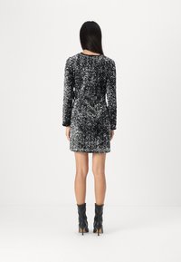 Μαύρο και ασημένιο φόρεμα με παγιέτες, με μακριά μανίκια, εφαρμοστή γραμμή και στρογγυλή λαιμόκοψη, σε συνδυασμό με μαύρες μπότες μέχρι τον αστράγαλο.