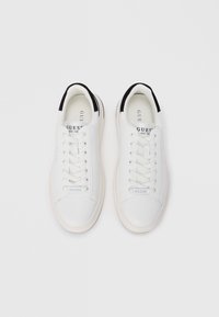 Baskets blanches avec une tige en cuir lisse, accents noirs sur le talon et une semelle en caoutchouc texturée. Design à lacets avec un détail logo sur le côté.
