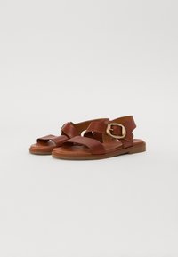 Brown leather sandals with cross straps and a buckled accent. Flat sole and open design for breathability. Textured surface with stitched detailing.