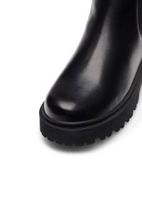 Čierna kožená členková obuv s okrúhlou špičkou, textúrovanou gumovou podrážkou a charakteristickým ryhovaným okrajom. Hladký povrch s minimálnym zdobením.