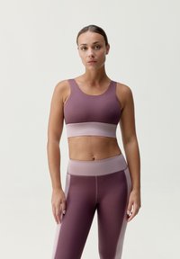 Fialová sportovní podprsenka a odpovídající legíny s jemným růžovým páskem. Materiály vypadají hladce, mají přiléhavý střih a minimální švy.