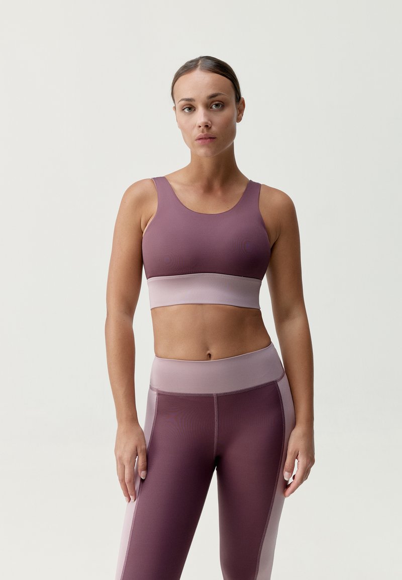 Fialová sportovní podprsenka a odpovídající legíny s jemným růžovým páskem. Materiály vypadají hladce, mají přiléhavý střih a minimální švy.