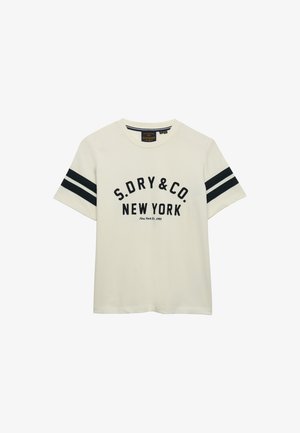 Camiseta de color crema de manga corta con doble rayas negras en las mangas y texto negro "S.DRY&CO. NEW YORK" en la parte delantera.