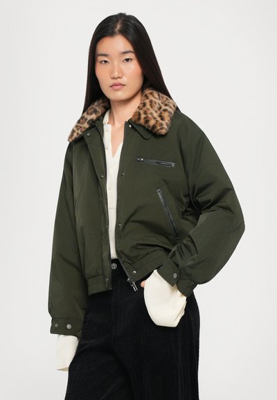 Olive krāsas bomber jaka ar leopardu raksta mākslīgās kažokādas apkakli, ar priekšējiem rāvējslēdzēja kabatām un ribinātām piedurknēm. Modelis valkā gaišu krekliņu zem tās.